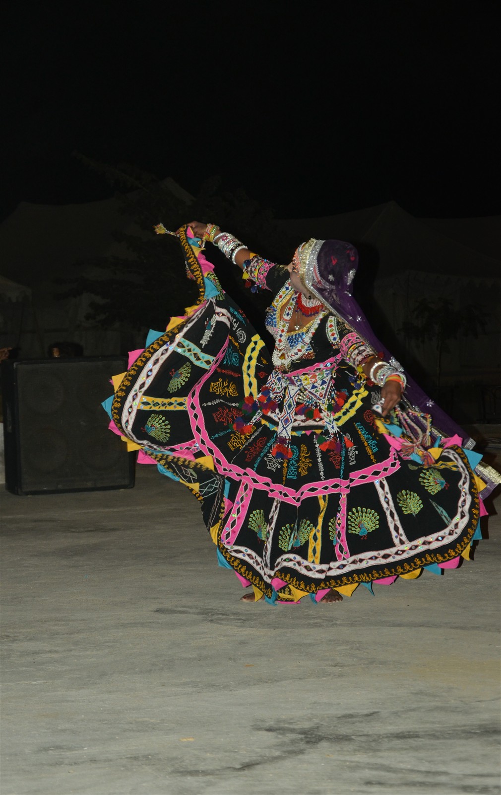 A Kalbelia performer dancing outdoors in an embroidered black skirt in a desert setting